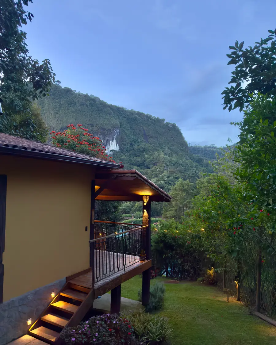 Chalé Lua Nova ao entardecer com luzes acesas e as montanhas ao fundo
