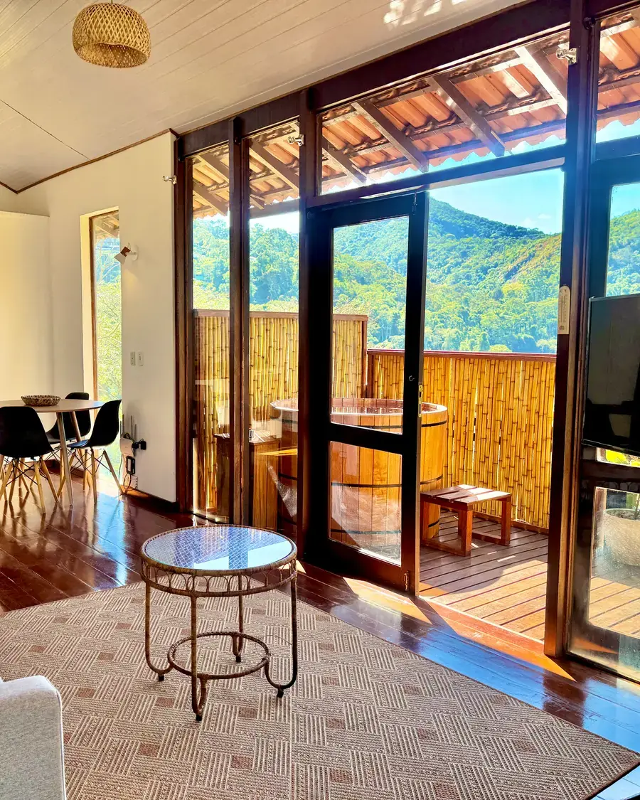 Sala da Cabana Orion abrindo para o deck com ofurô e vista para as montanhas de Itaipava