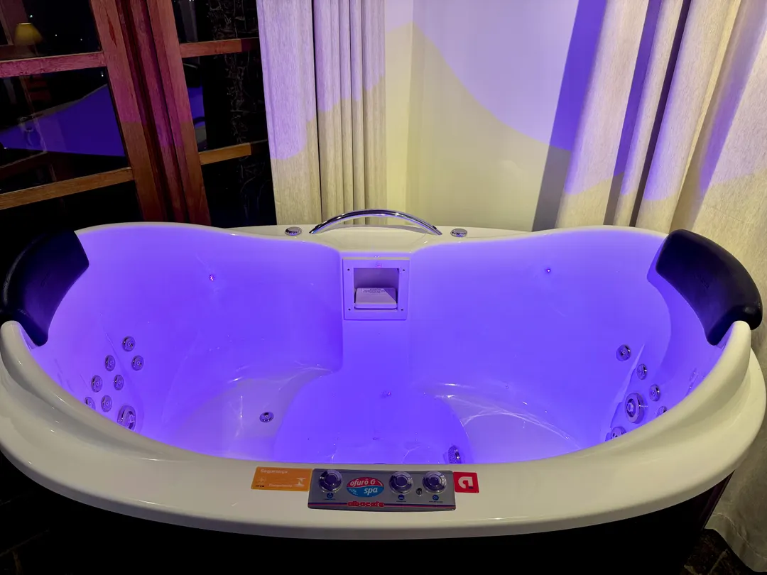 Ofurô com cromoterapia iluminado em roxo no quarto do Refúgio Céu Azul