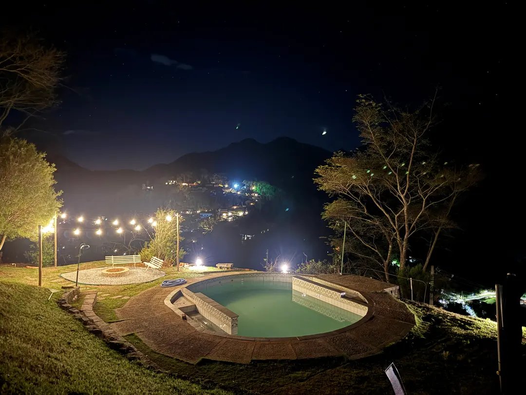 Jardim do Refúgio Céu Azul à noite, com luzes penduradas e a piscina iluminada ao fundo