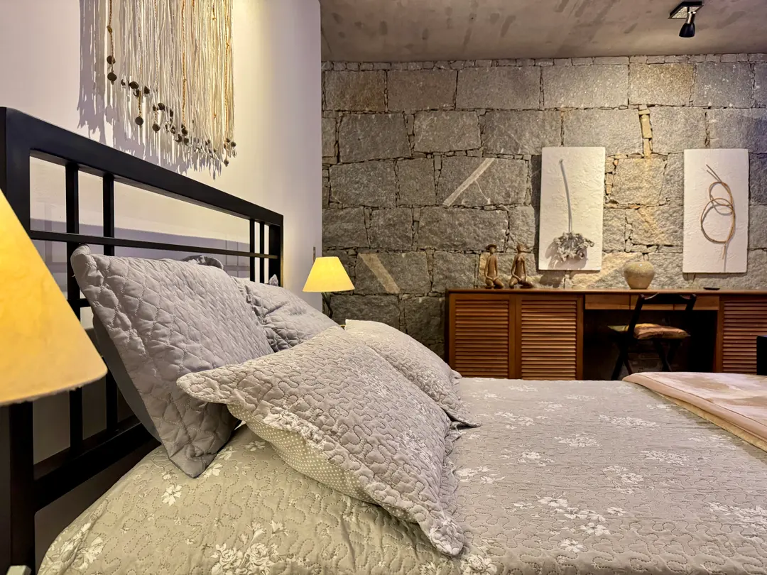 Quarto do Refúgio Céu Azul com parede de pedra aparente, TV e cômoda de madeira