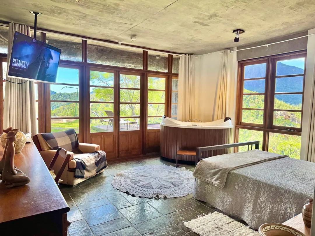 Sala de estar do Refúgio Céu Azul com poltronas, TV e portas de vidro para o jardim