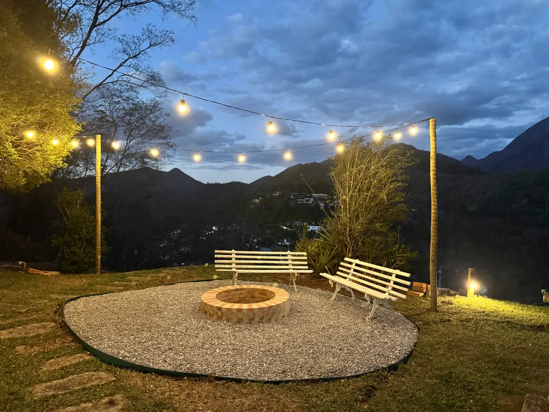 Roda de fogueira à noite no Refúgio Céu Azul, com bancos brancos e luzes penduradas