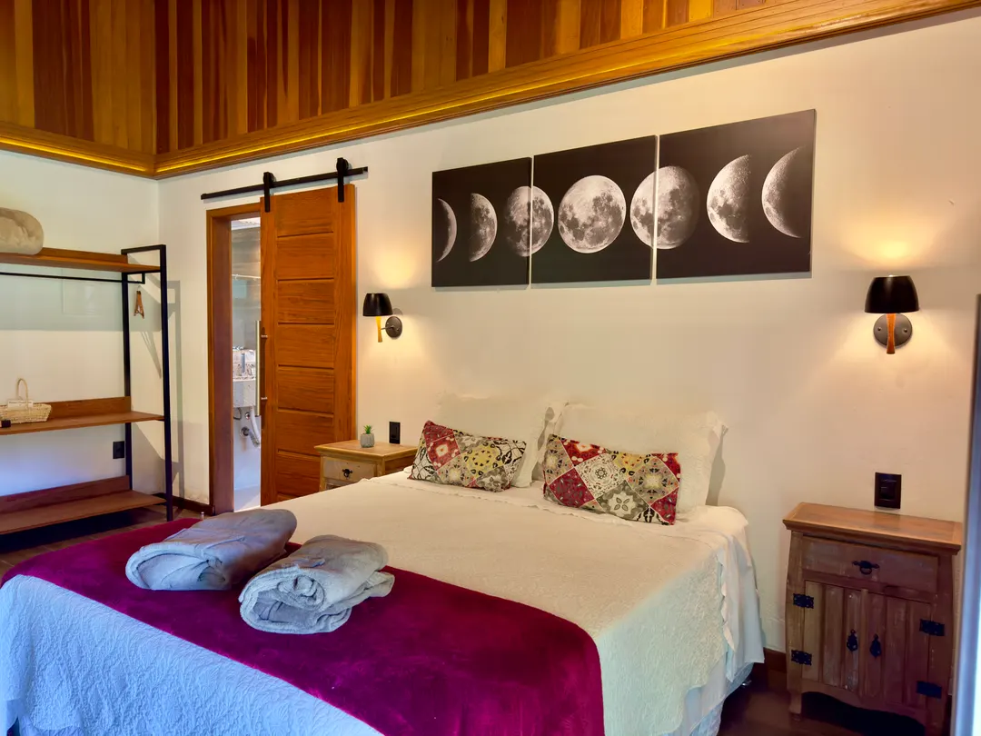 Cama de casal do Chalé Lua Nova com arte das fases da lua na parede