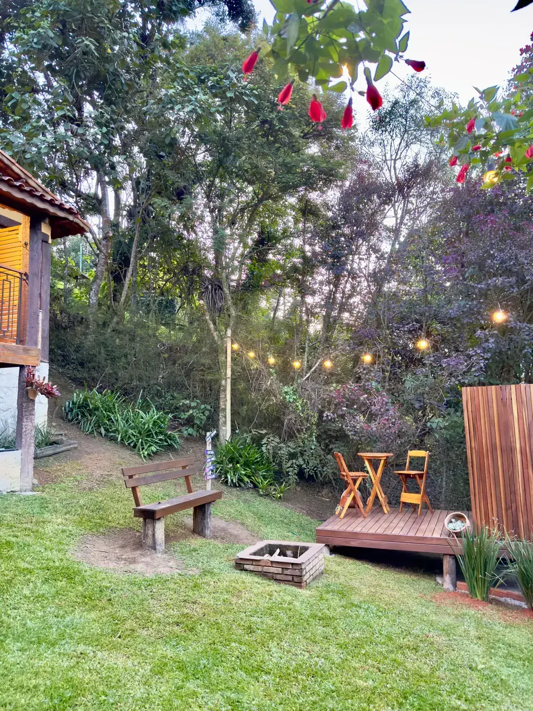 Jardim do Chalé ao entardecer, com banco de madeira, fogueira e luzes penduradas nas árvores