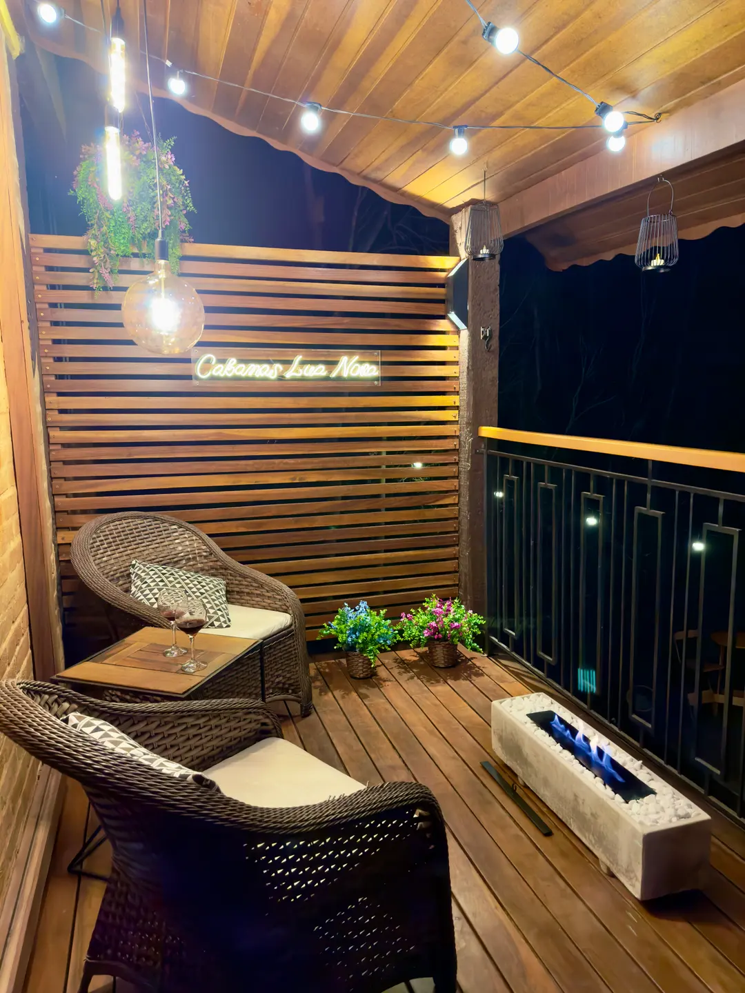 Poltronas de vime no deck coberto do Chalé à noite, com letreiro Cabanas Lua Nova aceso