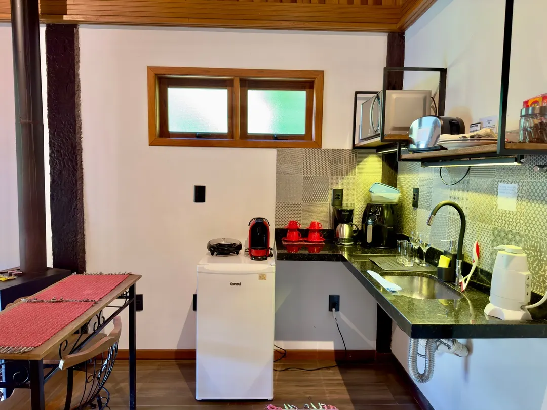 Cozinha de apoio do Chalé, com mini geladeira, cafeteira e grill elétrico sobre bancada de granito