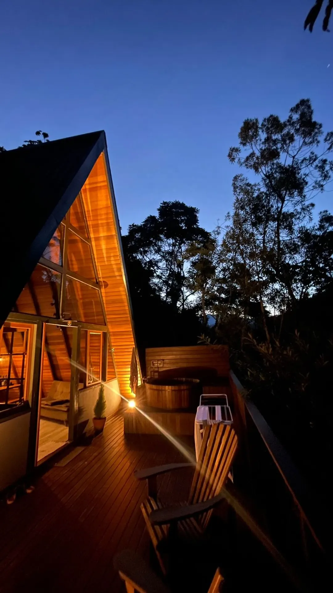 Cabana Solaris, A-frame de madeira ao anoitecer, com luz quente acesa e ofurô no deck