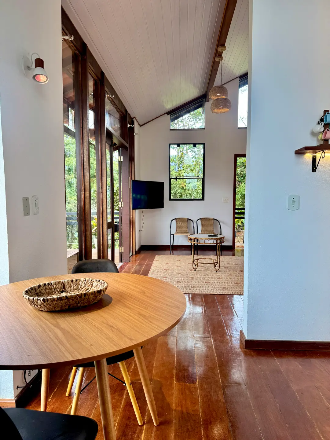 Sala de estar da Cabana Orion com mesa redonda, cadeiras de vime e portas de vidro abertas pro deck