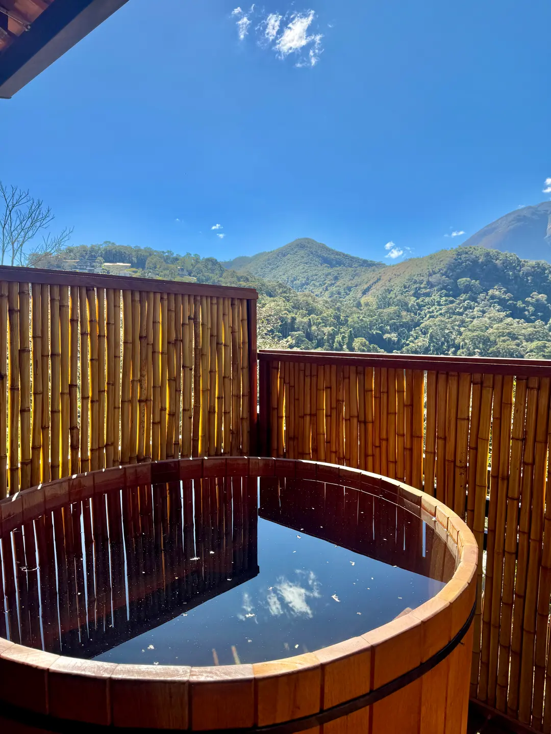 Ofurô privativo da Cabana Orion emoldurado por tela de bambu, com o céu azul de Itaipava ao fundo