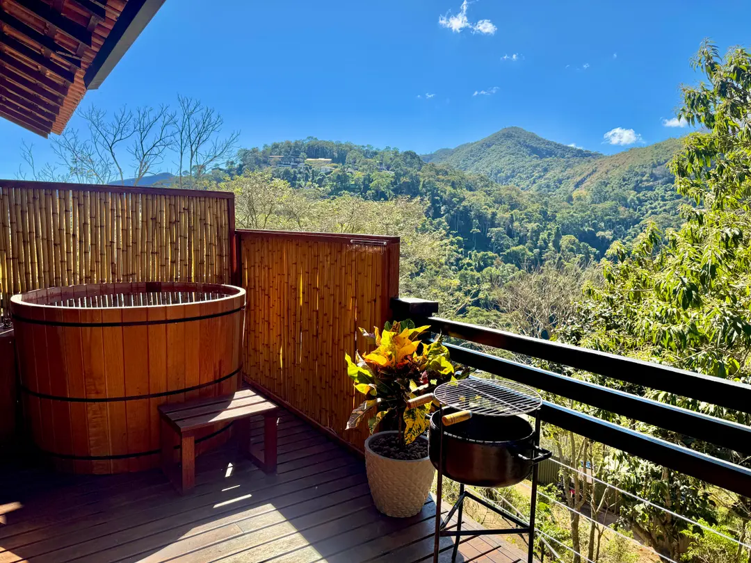Banco de madeira e vaso de flores ao lado do ofurô da Cabana Orion, com vista para a serra
