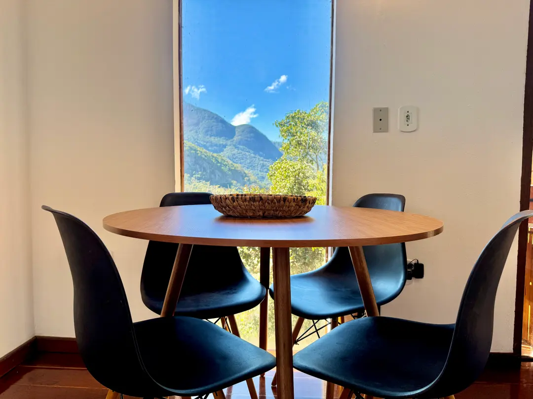 Mesa de jantar redonda da Cabana Orion com cadeiras pretas, janela emoldurando a serra