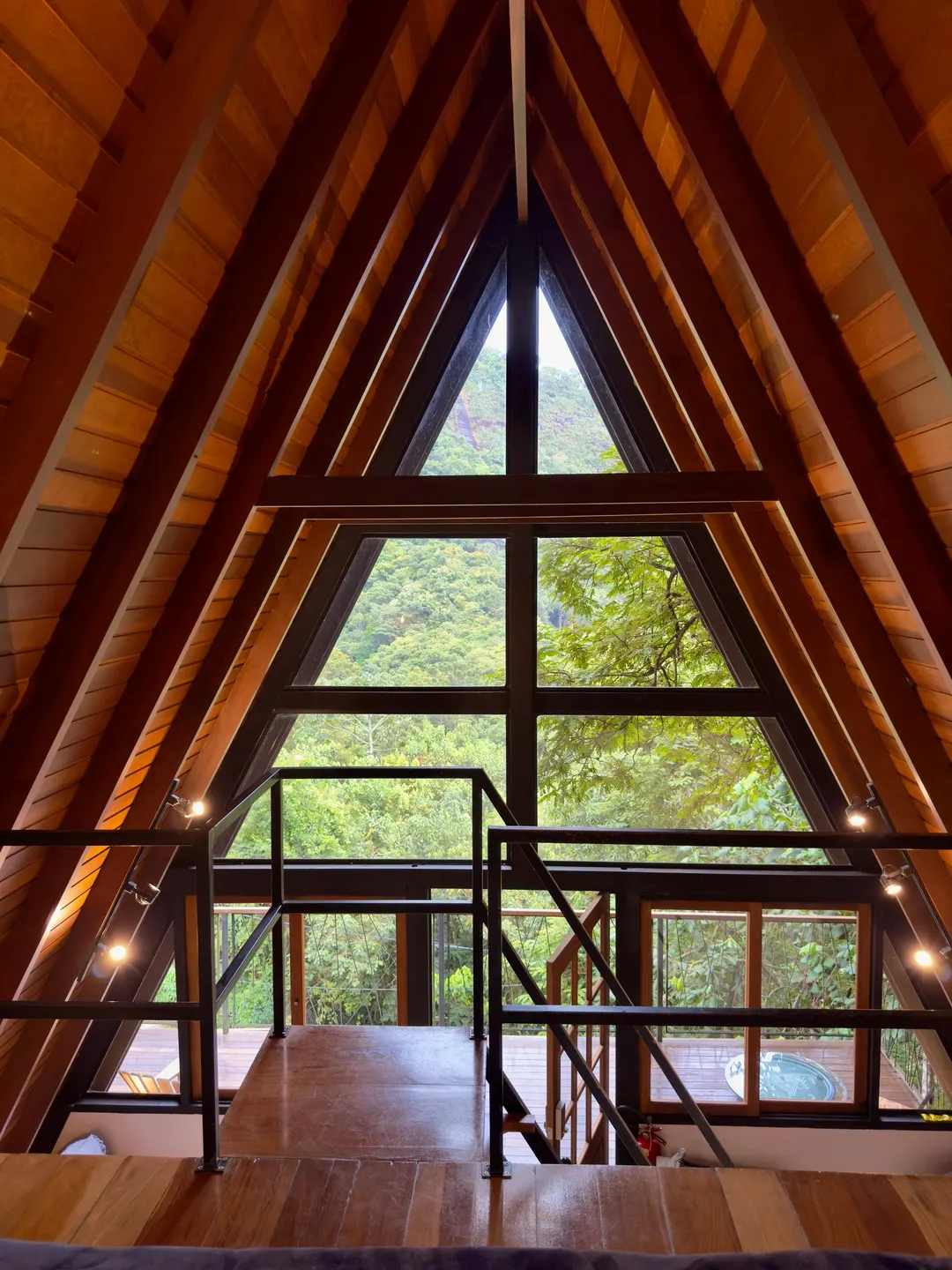 Interior da Cabana Sirius em contraluz, estrutura A-frame emoldurando a janela com vista para a mata