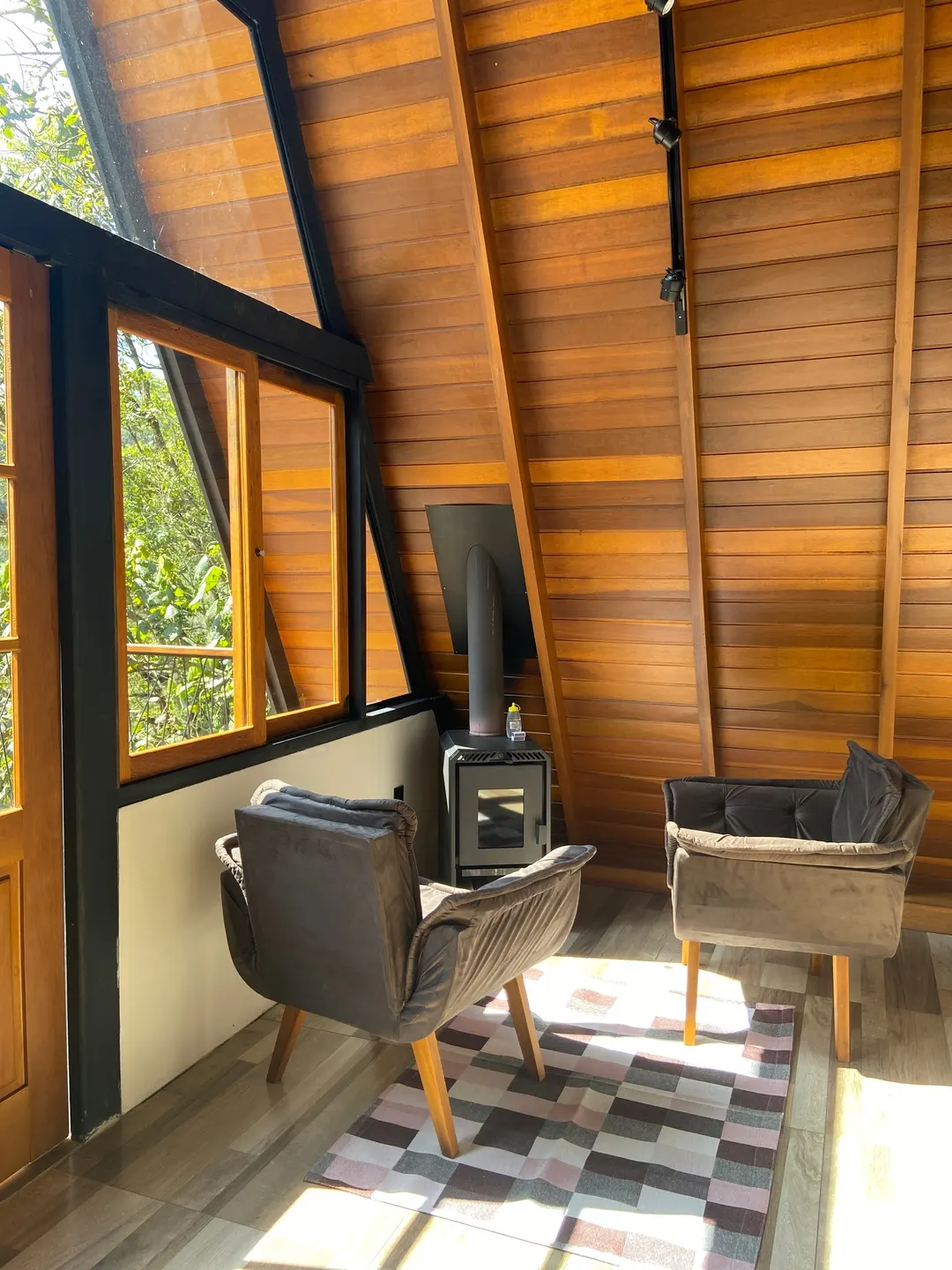 Calefator a lenha aceso na sala da Cabana Sirius, poltronas ao lado sob luz baixa
