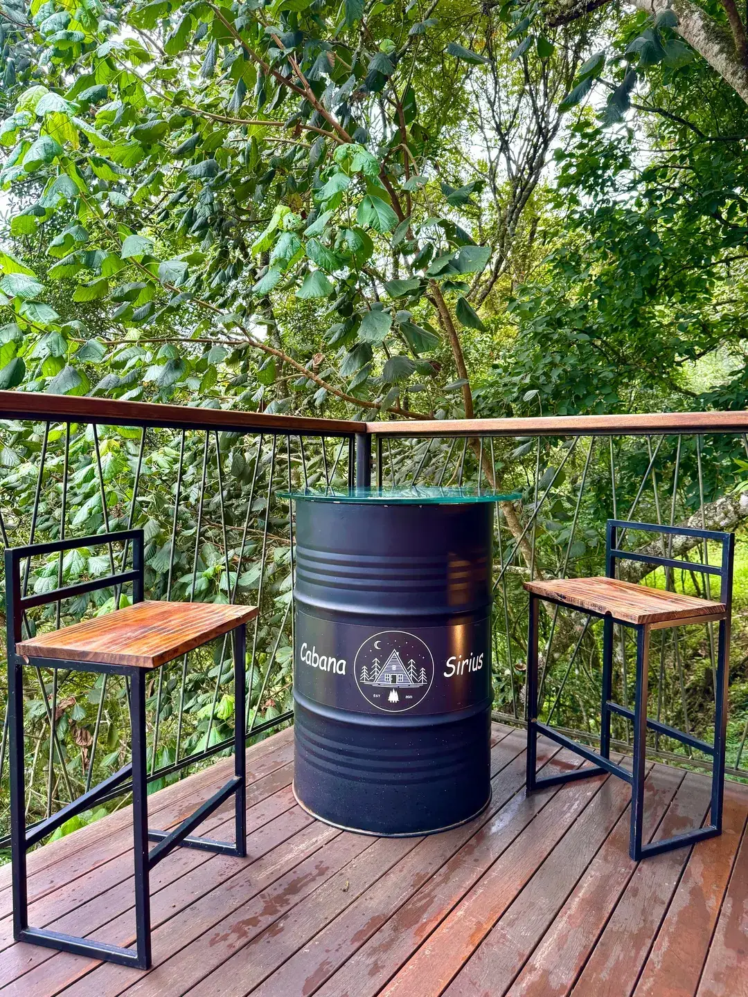 Mesa de barril de madeira com dois bancos no deck da Cabana Sirius, ao entardecer