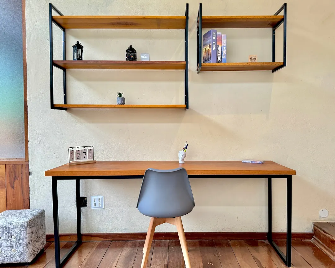 Escritório envidraçado do Studio Lua Nova, com mesa de trabalho, cadeira e estantes de madeira