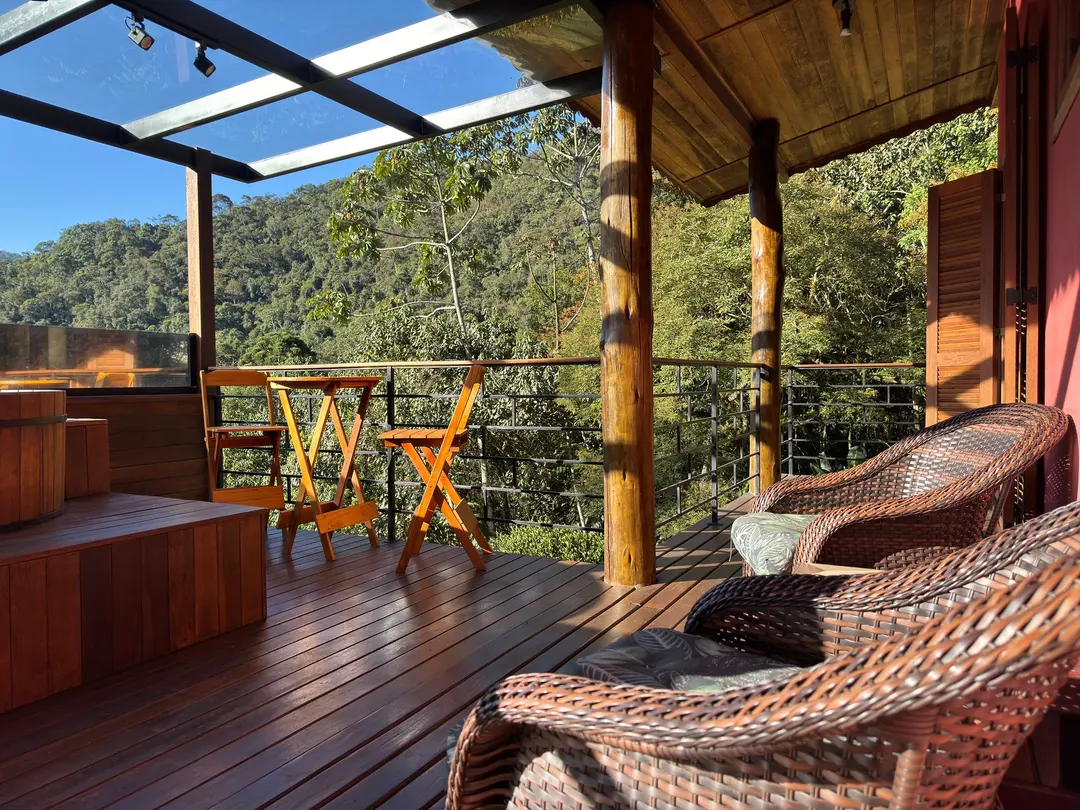 Deck coberto de vidro do Studio Lua Nova com poltronas de vime e vista para a mata